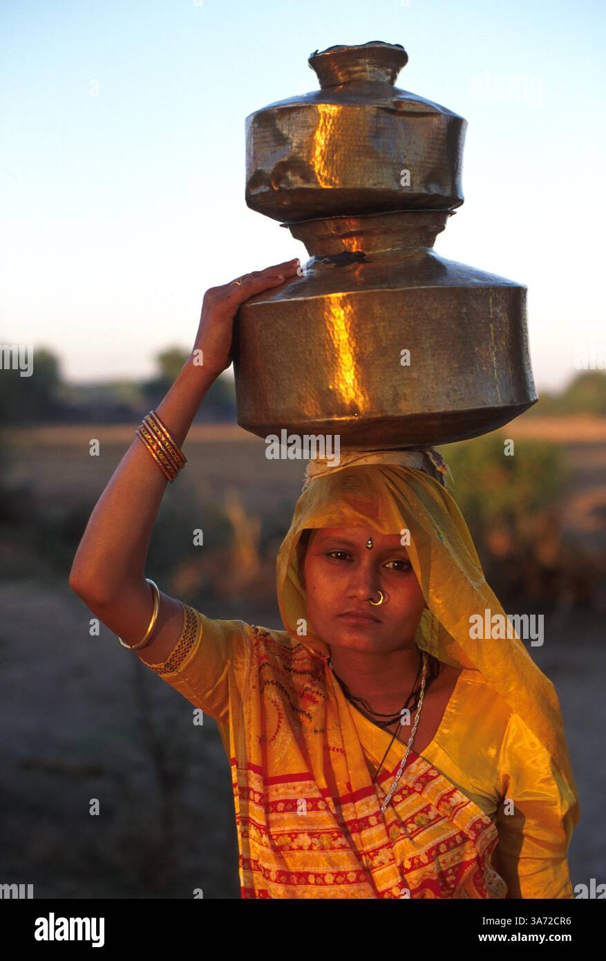 JANVIER 1, 2011 - CETTE FEMME DU VILLAGE DANS UN SARI PLUTÔT QUE LES VÊTEMENTS NOMADES TRADITIONNELS CHARGE LA TÊTE DES RÉCIPIENTS DE LAIT. CES CONTENEURS EN LAITON SONT REMPLIS ET AMENÉS À LA COOPÉRATIVE LAITIÈRE DU VILLAGE DEUX FOIS PAR JOUR, APRÈS LA TRAITE DE SON BÉTAIL. GUJURAT EST UN IMPORTANT PRODUCTEUR DE PRODUITS LAITIERS ET CHOCOLATÉS. ICI, DANS LE VILLAGE DE RUN DANS LA CAMPAGNE DE L'ÉTAT DE GUJURAT, À ENVIRON 60 MILES AU SUD D'AHMEDABAD. CE VILLAGE ABRITE UN PEUPLE BERGER NOMADE TRADITIONNEL QUI EN RAISON DU MANQUE DE TERRES DE PÂTURAGE OG POUR LEUR BÉTAIL SONT DEVENUS Banque D'Images