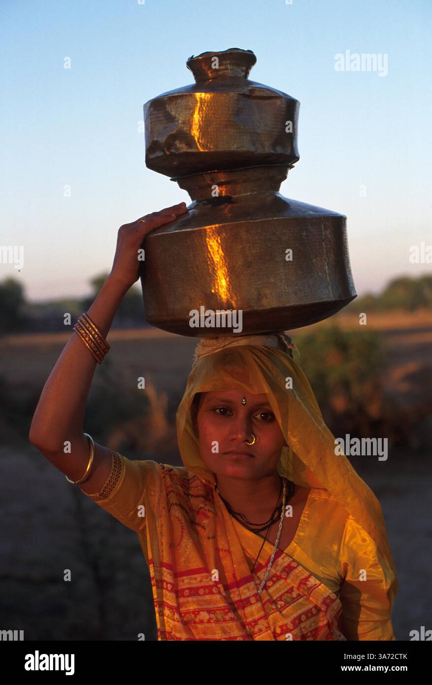 JANVIER 1, 2011 - CETTE FEMME DU VILLAGE DANS UN SARI PLUTÔT QUE LES VÊTEMENTS NOMADES TRADITIONNELS CHARGE LA TÊTE DES RÉCIPIENTS DE LAIT. CES CONTENEURS EN LAITON SONT REMPLIS ET AMENÉS À LA COOPÉRATIVE LAITIÈRE DU VILLAGE DEUX FOIS PAR JOUR, APRÈS LA TRAITE DE SON BÉTAIL. GUJURAT EST UN IMPORTANT PRODUCTEUR DE PRODUITS LAITIERS ET CHOCOLATÉS. ICI, DANS LE VILLAGE DE RUN DANS LA CAMPAGNE DE L'ÉTAT DE GUJURAT, À ENVIRON 60 MILES AU SUD D'AHMEDABAD. CE VILLAGE ABRITE UN PEUPLE BERGER NOMADE TRADITIONNEL QUI EN RAISON DU MANQUE DE TERRES DE PÂTURAGE OG POUR LEUR BÉTAIL SONT DEVENUS Banque D'Images