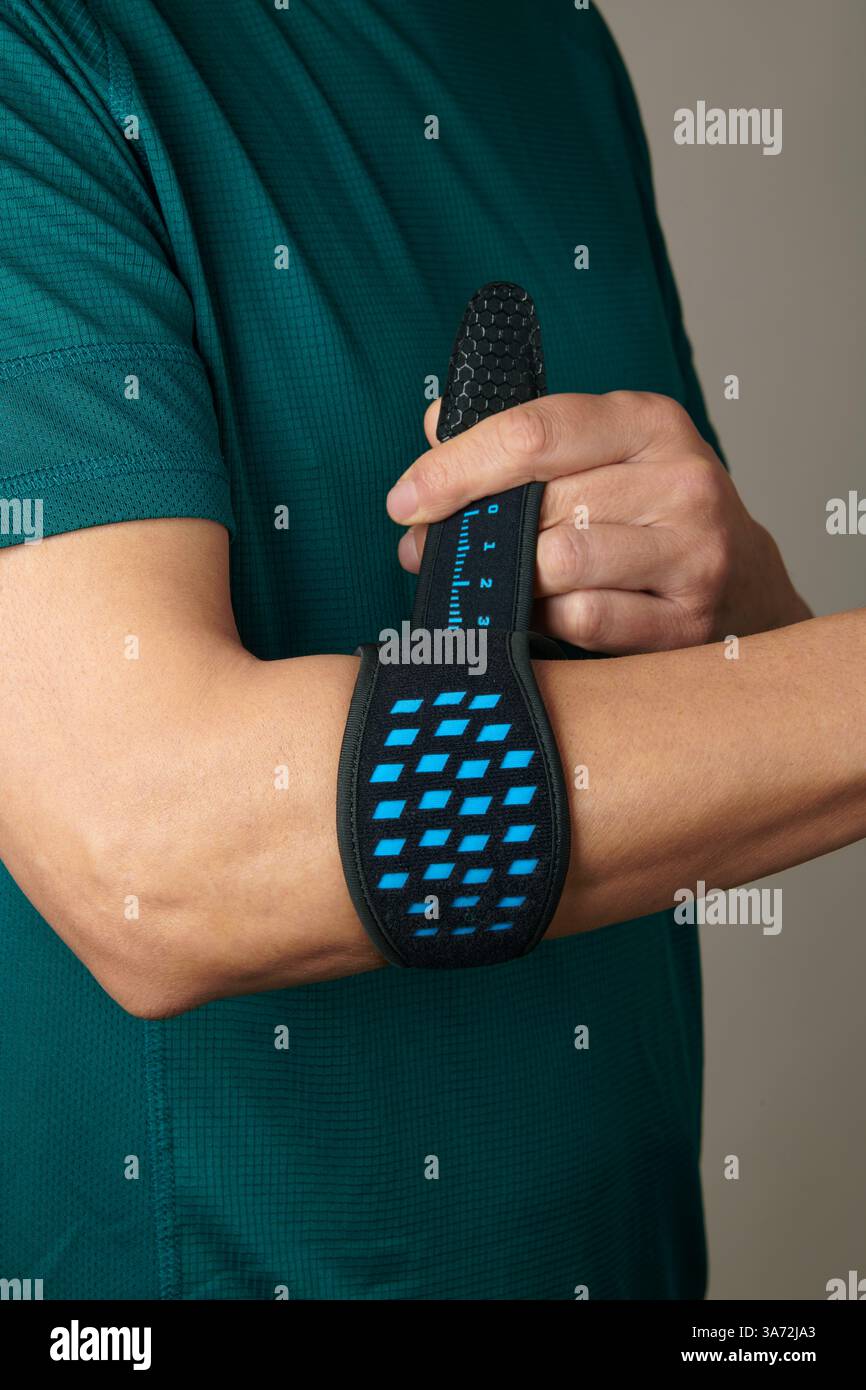 gros plan d'un homme portant un t-shirt de sport vert ajustant son bracelet épicondylite sur son bras, pour soulager la douleur de l'épicondylite Banque D'Images