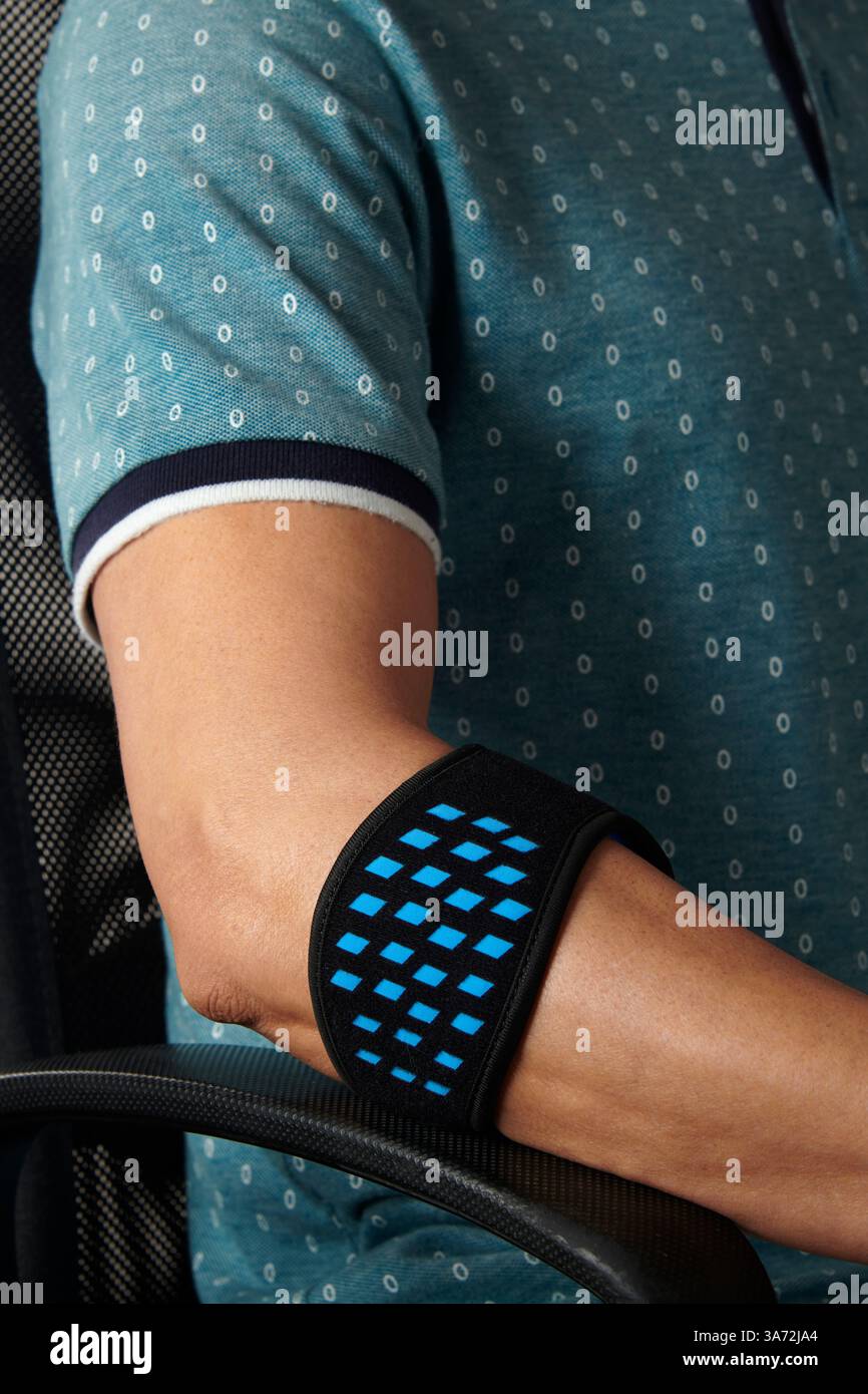 gros plan d'un homme portant un bracelet d'épicondylite sur son bras, pour soulager la douleur de l'épicondylite, alors qu'il est assis à son bureau Banque D'Images