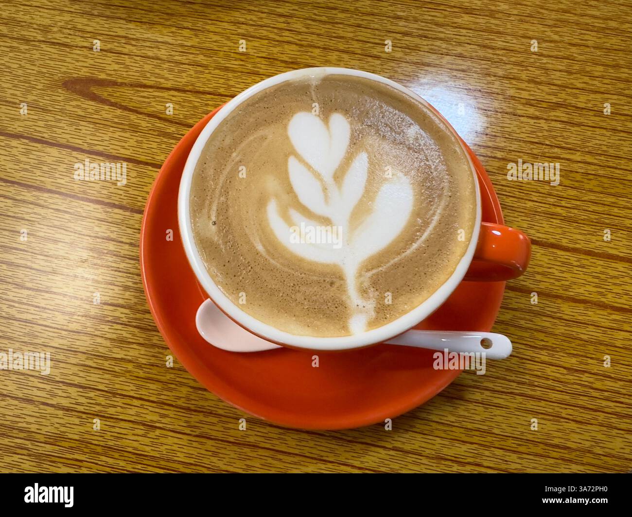 Délicieux café avec latte art servi dans une tasse d'orange vibrante dans un café confortable. - Image de stock capturée avec un smartphone