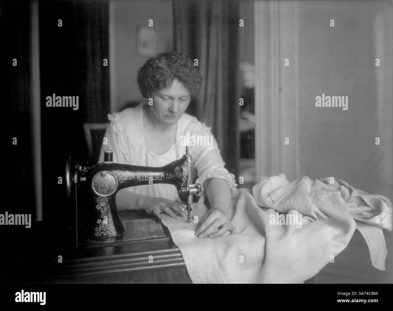 États-Unis - circa 1900 - Une femme utilise l'une des premières machines à coudre CHANTEUSE vers 1900. L'invention des machines à coudre Singer est devenue un p industriel Banque D'Images