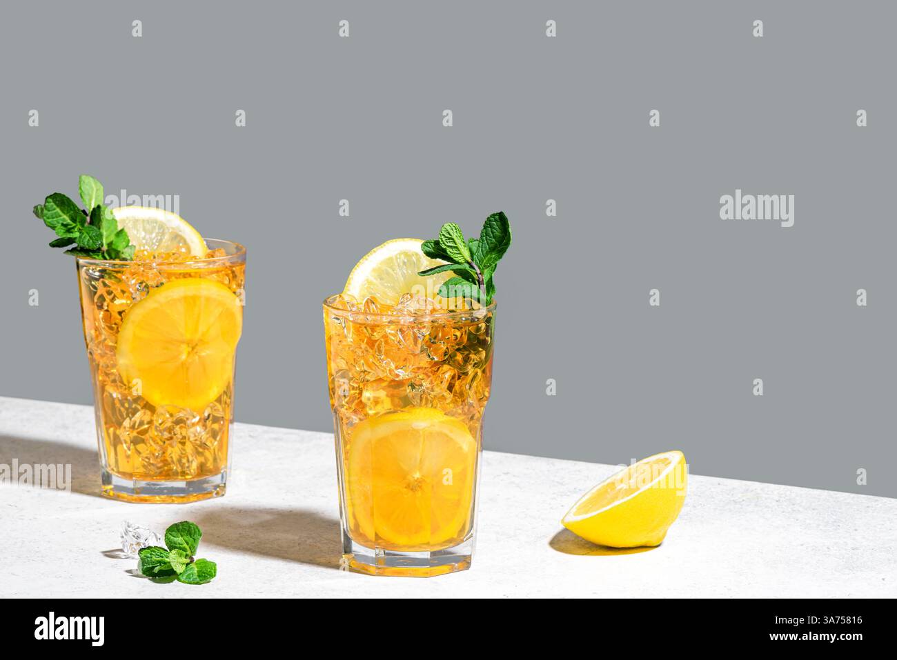 Thé glacé au citron. Deux verres de thé glacé avec des tranches de citron, de la menthe et des glaçons sur fond blanc et gris, lumière dure à la mode avec des ombres, copie Banque D'Images
