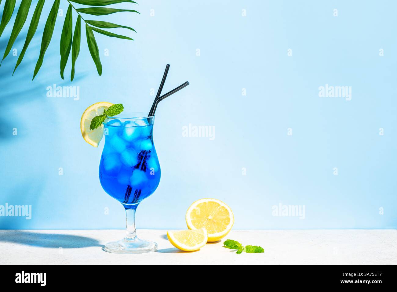 Cocktail d'été Blue Lagoon avec menthe et citron sur fond de ciel bleu avec feuille de palmier, espace copie. Concept de cocktail créatif tendance. Cocktail dr. Banque D'Images