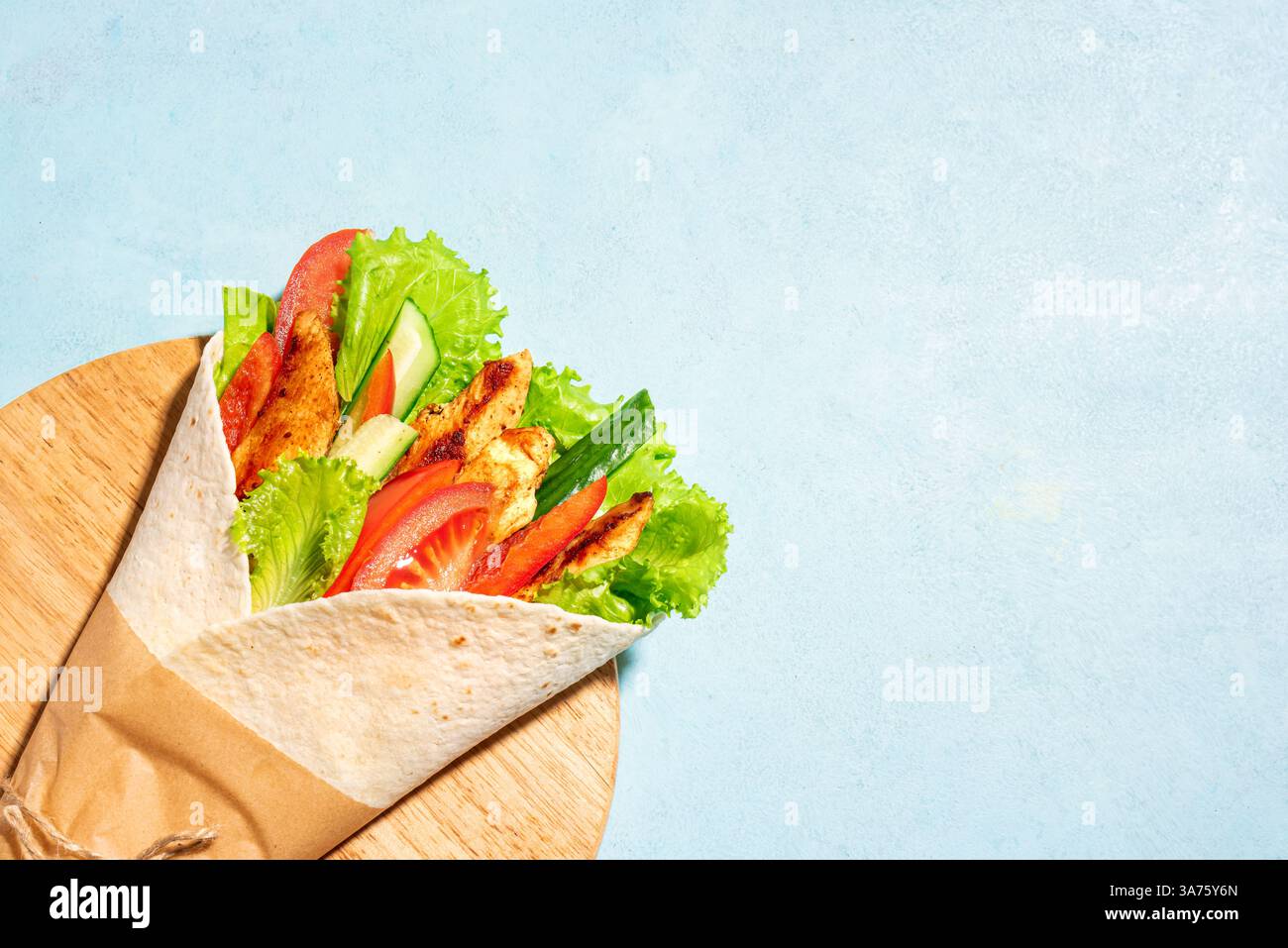 Sandwich au poulet enveloppé de tortilla avec des légumes sur fond bleu, espace de copie. Shawarma frais ou papier à base de fajita. Banque D'Images