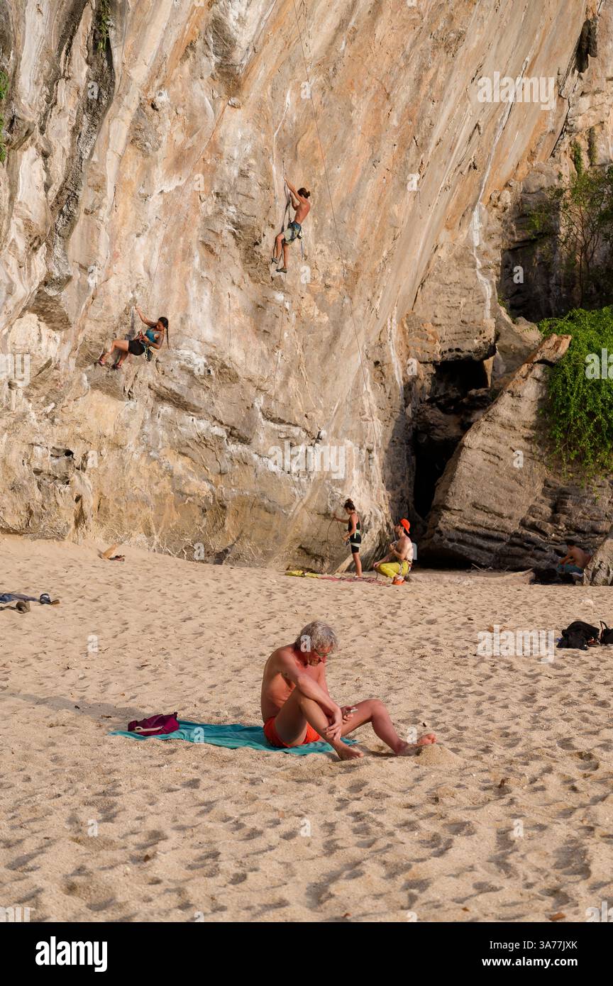 Les grimpeurs escaladent le mur de calcaire escarpé de la plage de Tonsai tandis qu'un ancien solarium se détend à proximité Banque D'Images