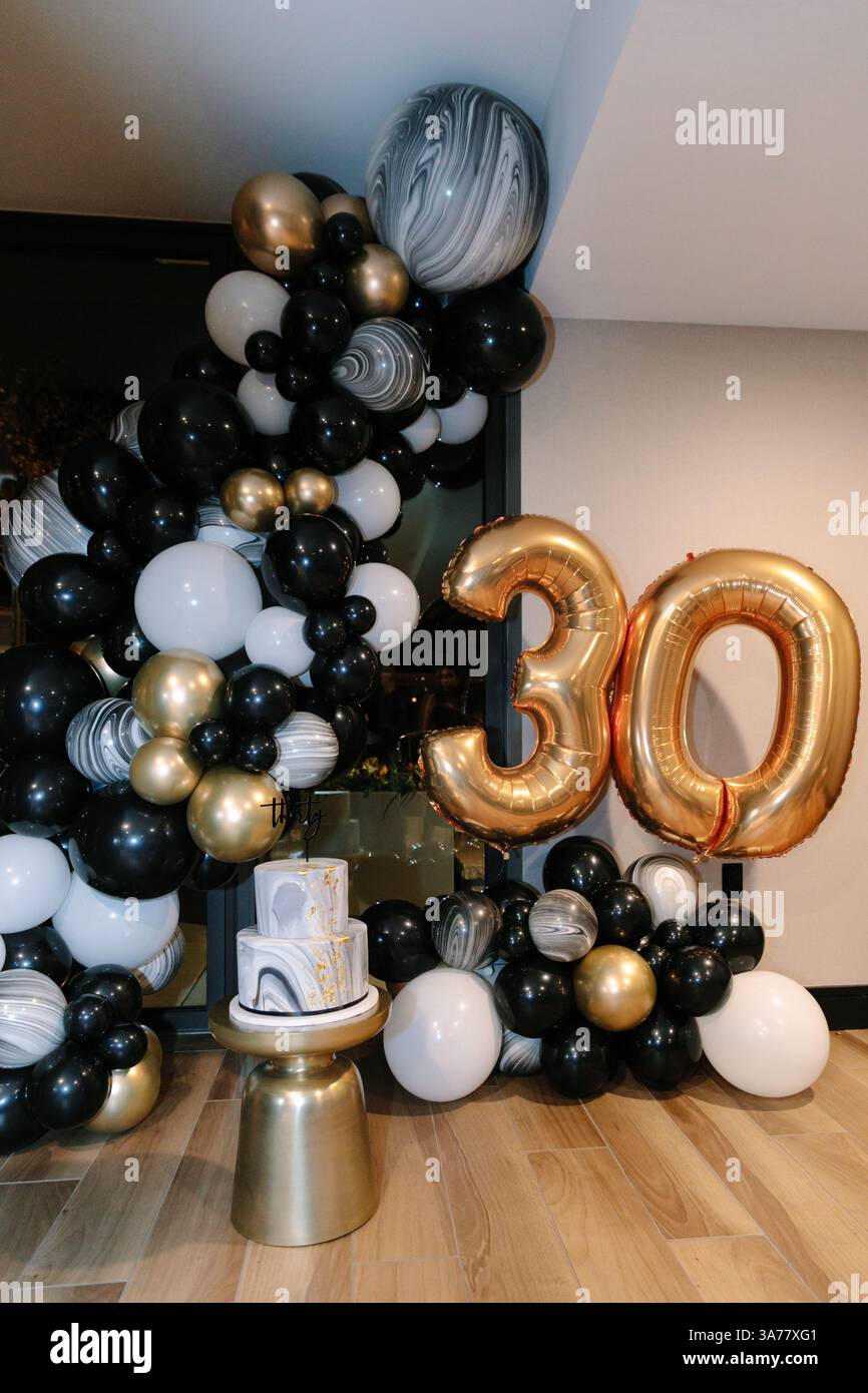 Configuration festive mettant en vedette un gâteau et de grands ballons marquant les trente ans dans un lieu intérieur élégant. Banque D'Images