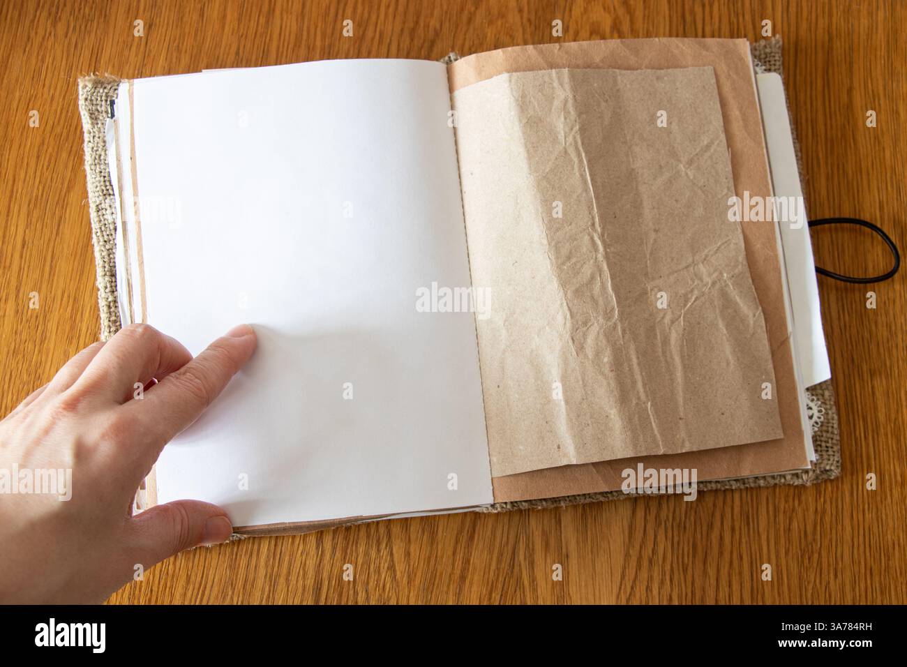 Main féminine pointant à la page dans un cahier blanc fait maison à partir de papier kraft et toile de jute sur une table en bois, cahier créatif Banque D'Images