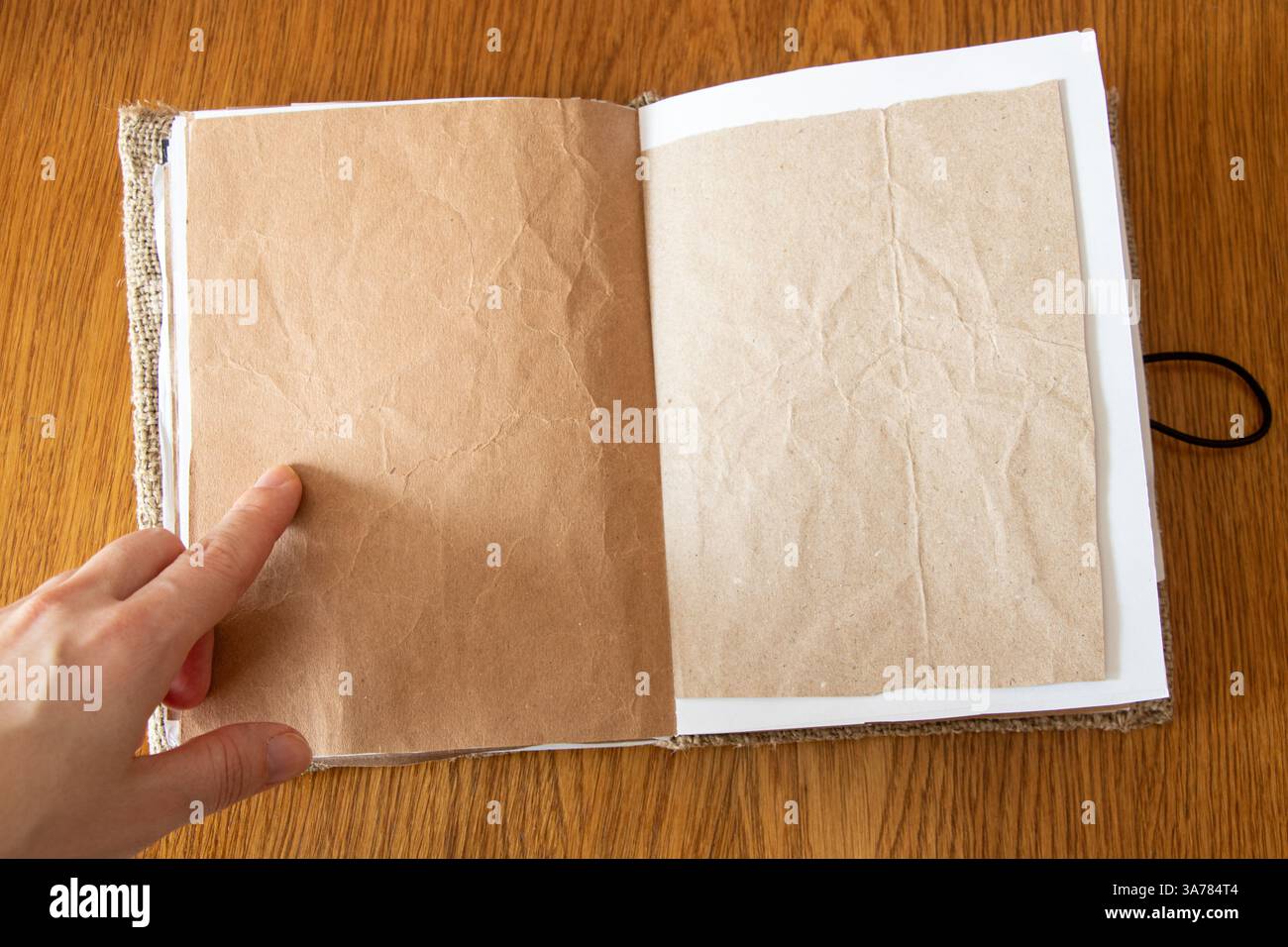 Main féminine pointant à la page dans un cahier blanc fait maison à partir de papier kraft et toile de jute sur une table en bois, cahier créatif Banque D'Images