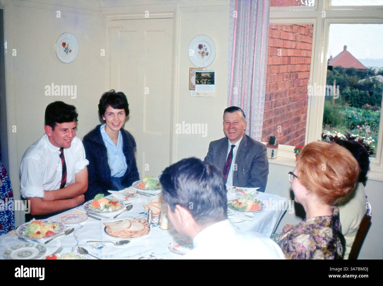 Un joyeux rassemblement familial britannique capturé en septembre 1963, alors qu'ils profitaient d'un repas de célébration ensemble. La scène, conservée sur un film de diapositives couleur 35 mm, offre un aperçu charmant de la vie quotidienne dans l'Angleterre des années 1960, avec de la porcelaine à motifs, des plats faits maison et des conversations chaleureuses. Banque D'Images