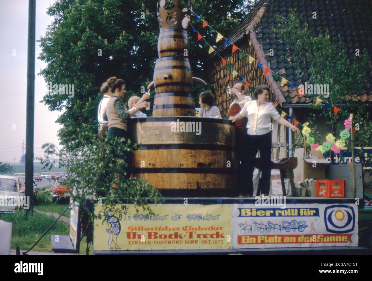 Un flotteur de défilé dynamique au 1974 Schützenfest à Aligse, en Allemagne, présente un baril de bière géant en bois entouré de célébrants. Le char, promouvant « Ur-Bock-Treck » d'Einbecker Bier d'Einbeck à Bonn (1873), est décoré de banderoles et de fleurs, capturant l'esprit festif et l'atmosphère communautaire de cet événement traditionnel allemand. Banque D'Images