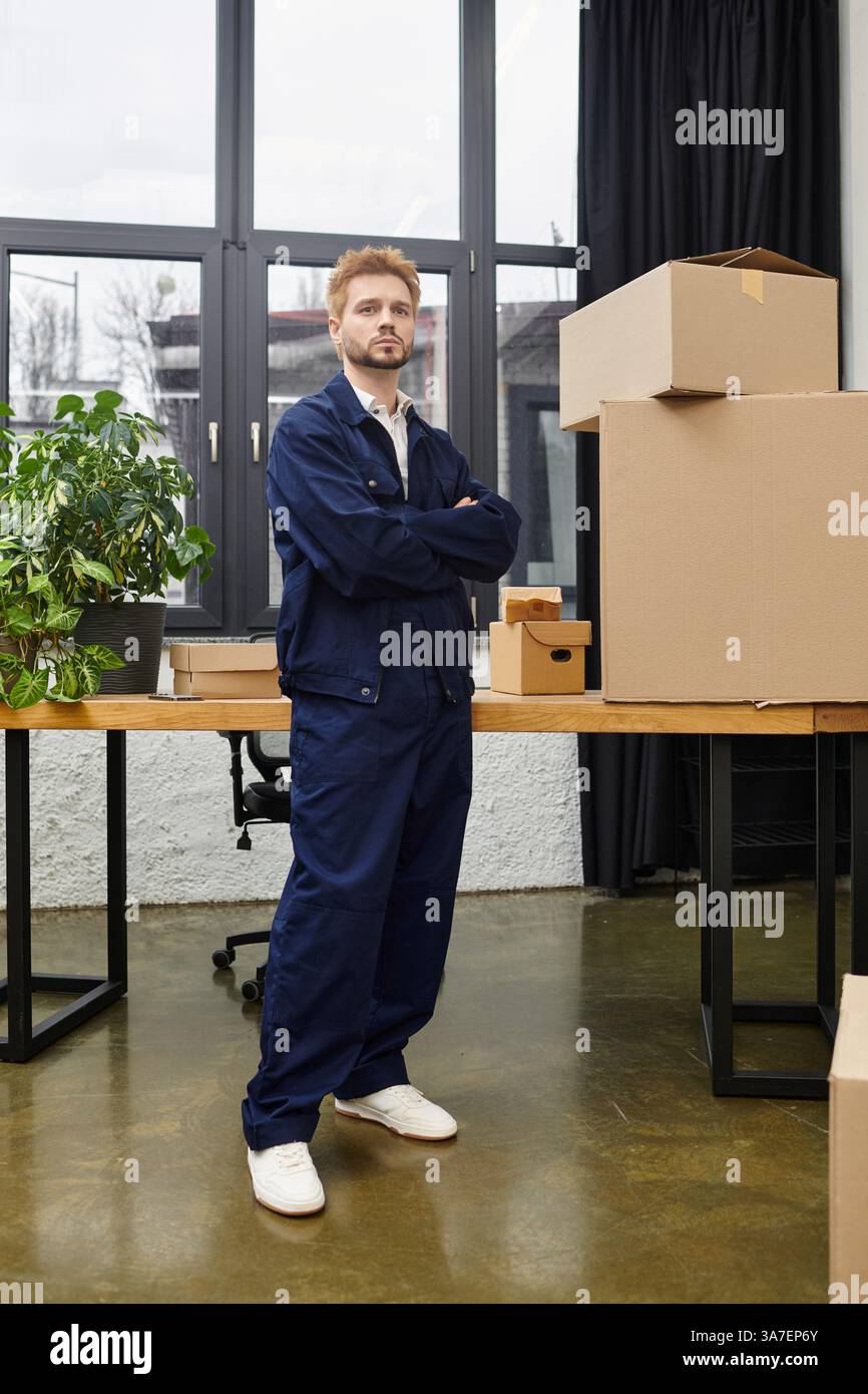 Un jeune homme se tient confiant dans un bureau contemporain, entouré de boîtes en carton et de plantes. Banque D'Images