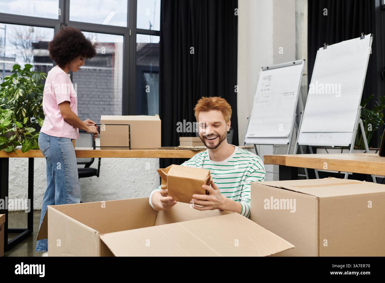 Deux personnes emballent et déballent volontiers des boîtes dans un bureau moderne. Banque D'Images