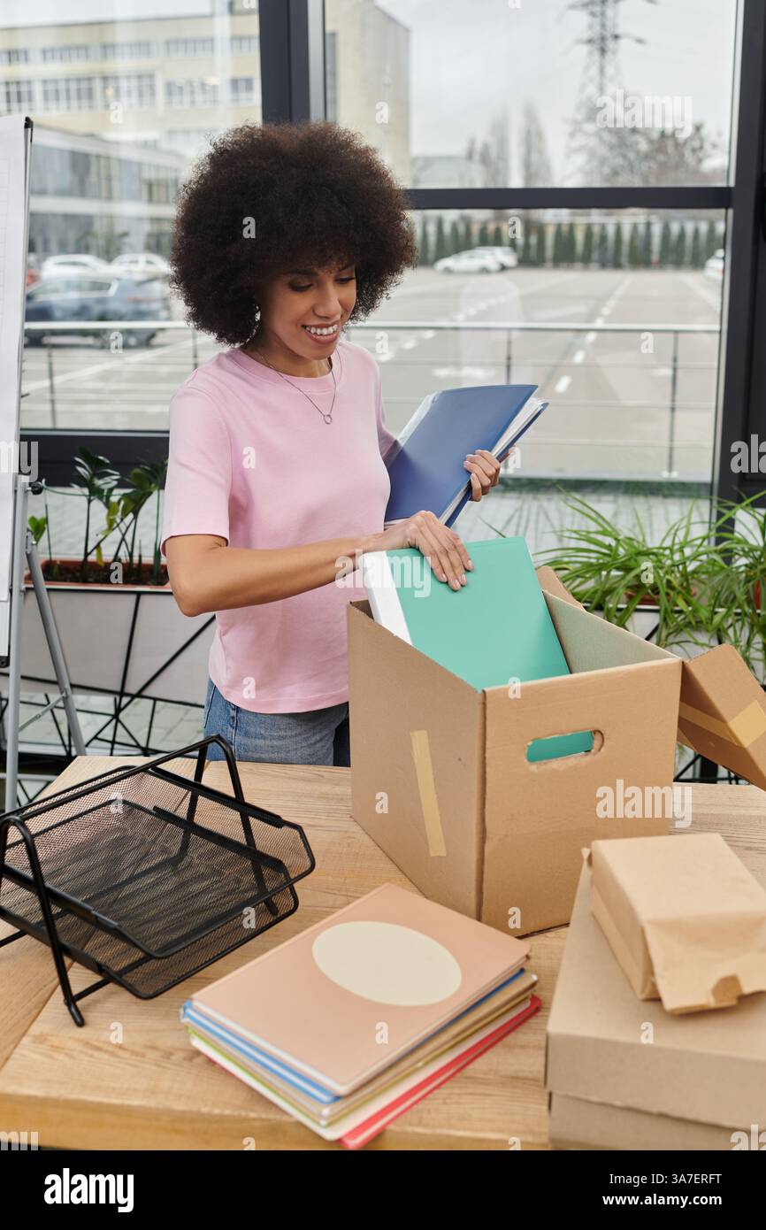 Une jeune femme trie avec enthousiasme sa boîte de fournitures tout en préparant son espace de travail. Banque D'Images