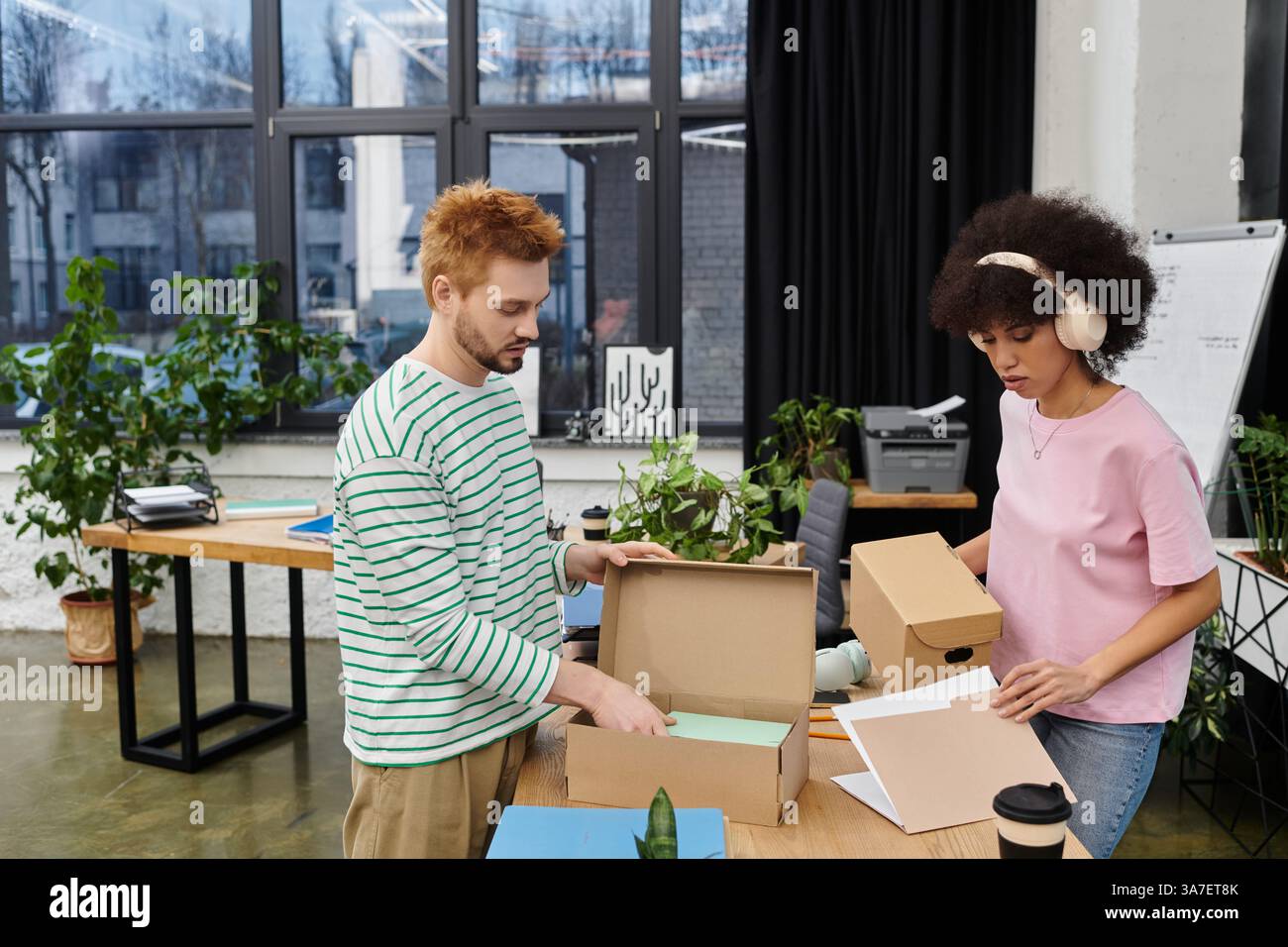 Deux personnes emballent et déballent dans un bureau moderne rempli de plantes. Banque D'Images