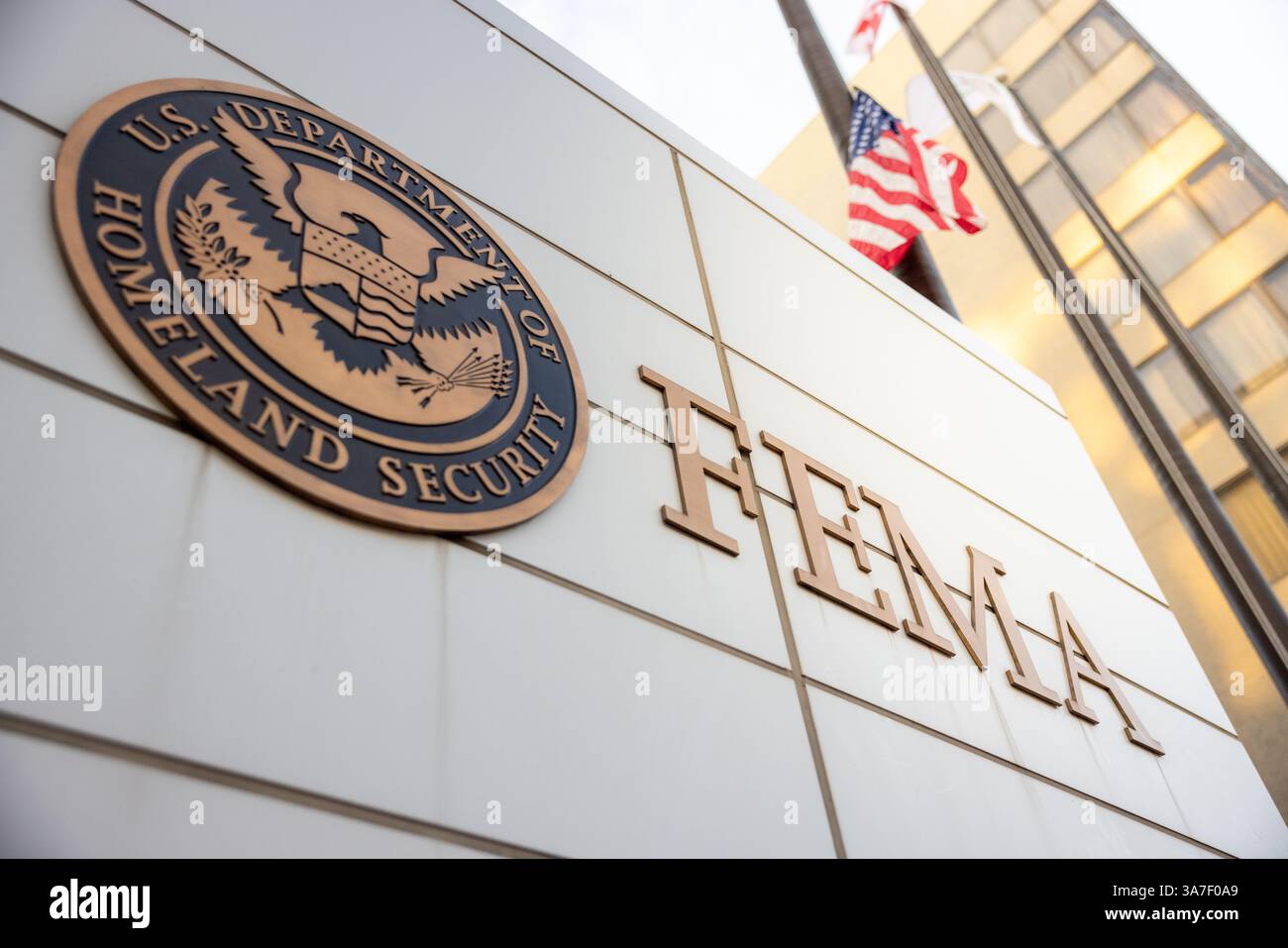 Signe FEMA (Federal Emergency Management Agency) et logo du département américain de la sécurité intérieure avec la lumière du soleil qui traverse les drapeaux américains derrière Banque D'Images