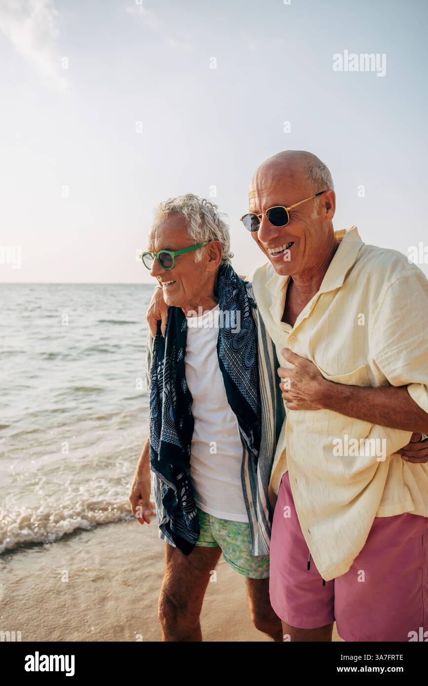 Heureux homme gay senior marchant avec le bras autour de petit ami sur la plage Banque D'Images