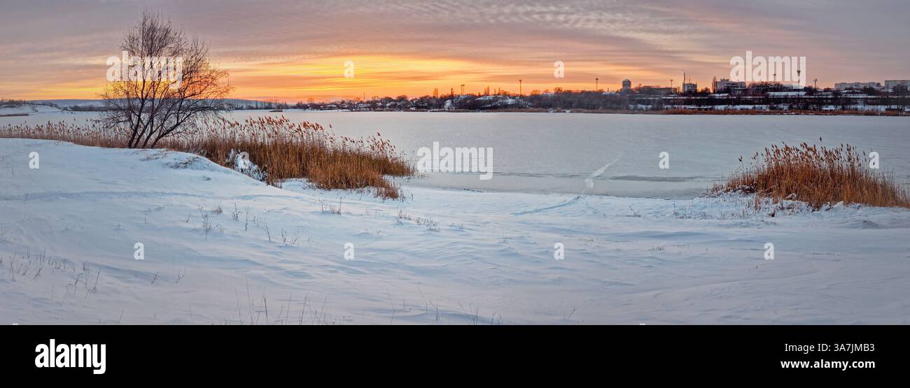 Coucher de soleil panoramique d'hiver au-dessus du lac Delia gelé dans la ville d'Ungheni, Moldavie. Belle scène d'hiver avec crépuscule coloré au-dessus de l'étang couvert de sn - Image de stock capturée avec un smartphone