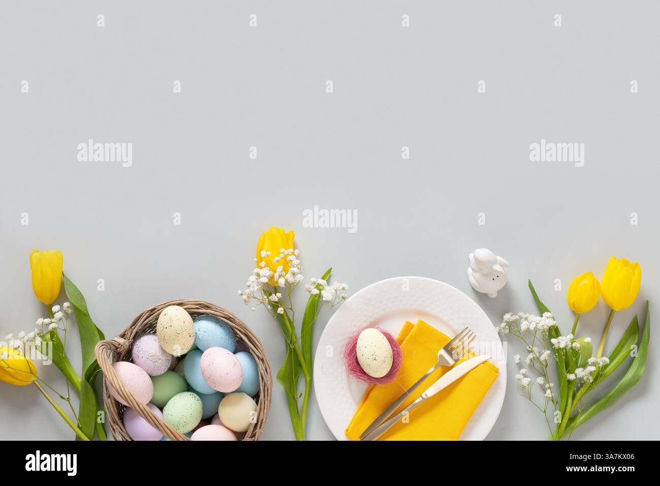 Cadre de Pâques avec des œufs jaunes pastel, des fleurs de tulipe, gypsophila et poussin jaune sur fond gris. Vue de dessus. Pose à plat. Joyeuses salutations de Pâques Banque D'Images