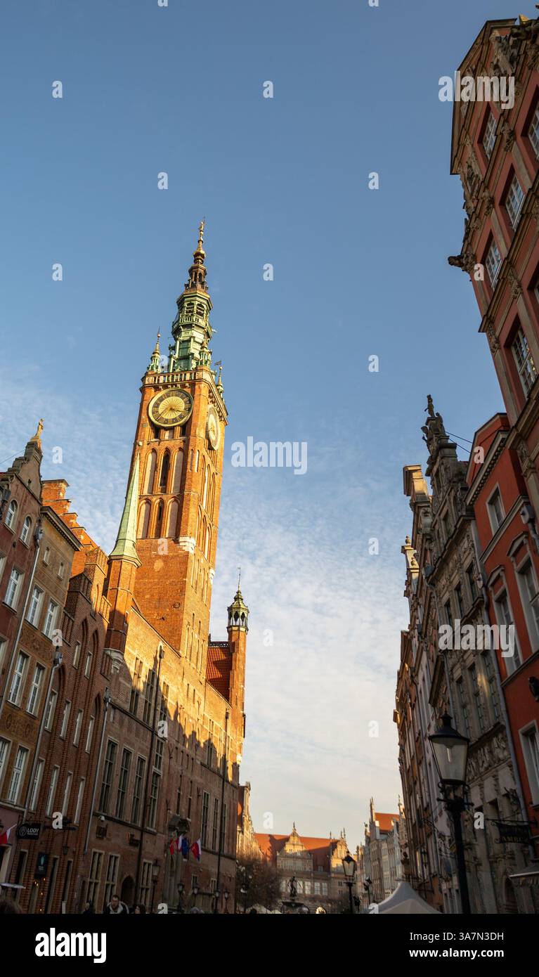 Tour de l'horloge historique baignée de lumière dorée, dominant les bâtiments européens traditionnels sous un ciel bleu clair Banque D'Images