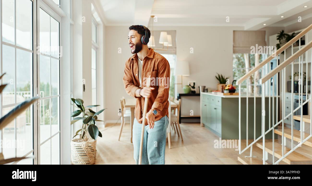 Balayer, musique et chanter avec l'homme à la maison pour les corvées, la responsabilité ou le nettoyage de printemps. Danse, écouteurs et balayage avec personne heureuse dans l'appartement Banque D'Images