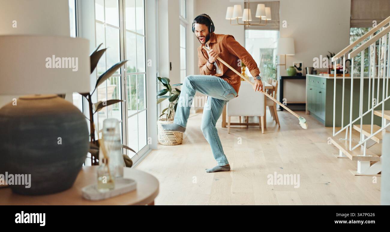 Énergie, musique et balayer avec l'homme à la maison pour les corvées, la responsabilité ou le nettoyage de printemps. Balai, danse et écouteurs avec personne excitée à l'intérieur Banque D'Images