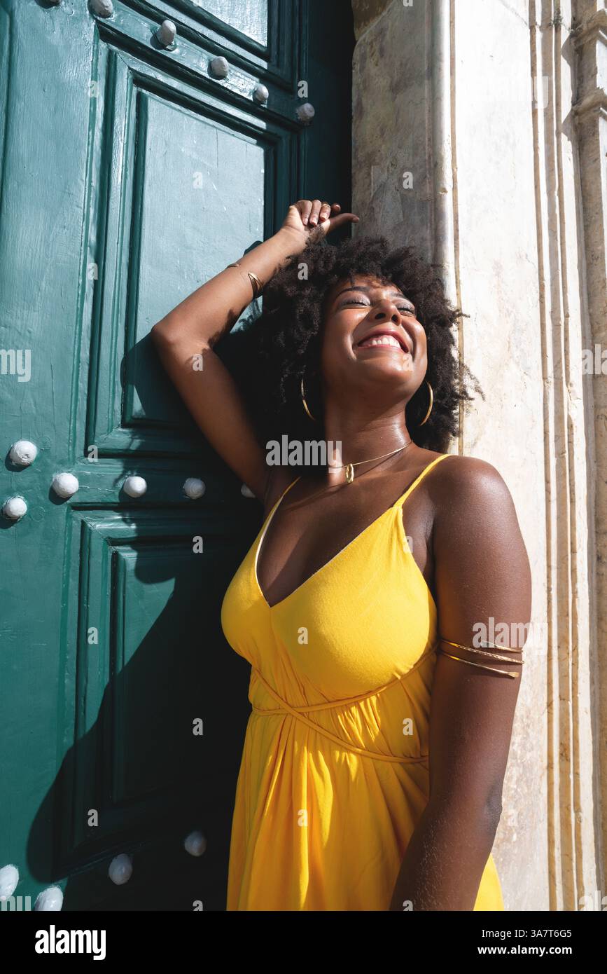 Belle femme noire avec des cheveux de corbeau portant une robe jaune posant pour la photo contre la grande porte verte de l'église. Heureux et souriant Banque D'Images