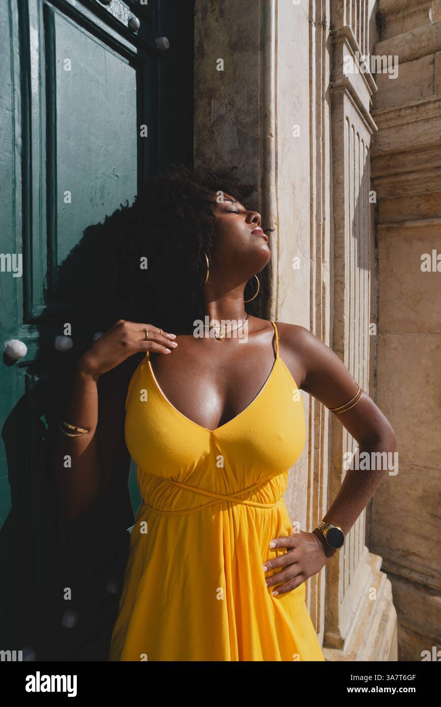 Belle femme noire avec des cheveux de corbeau portant une robe jaune posant pour la photo contre la grande porte verte de l'église. Heureux et souriant Banque D'Images