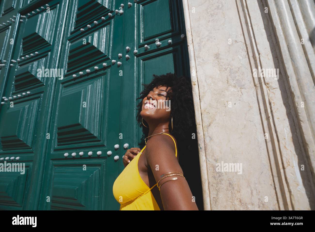 Belle femme noire avec des cheveux de corbeau portant une robe jaune posant pour la photo contre la grande porte verte de l'église. Heureux et souriant Banque D'Images