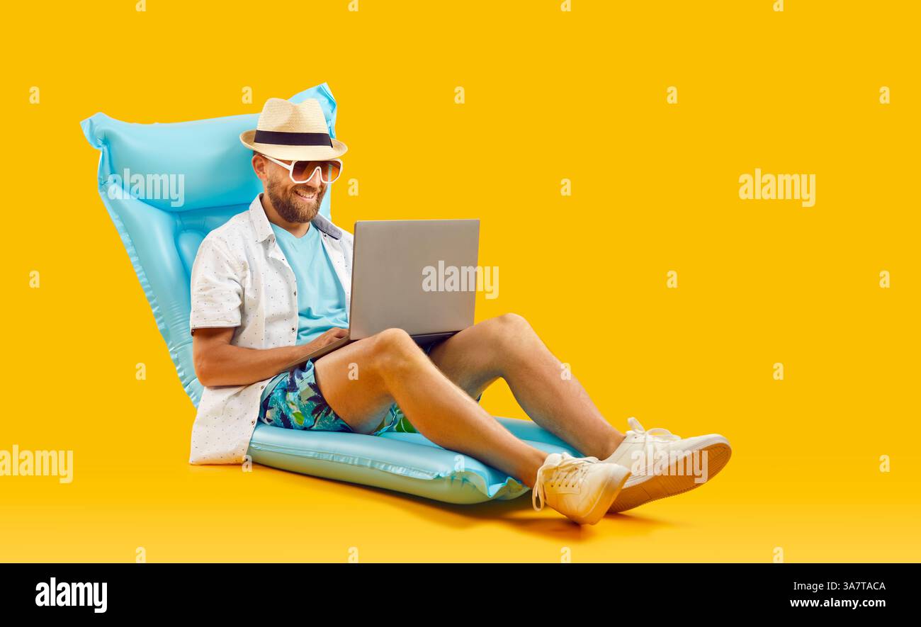 Homme heureux à la recherche de billets de mer et réservation d'hôtel tout en étant assis avec ordinateur portable sur matelas gonflable Banque D'Images