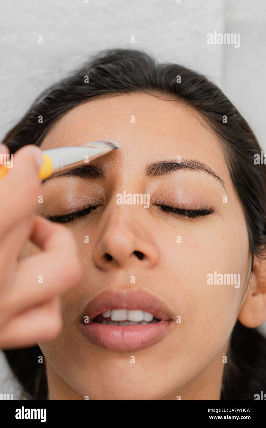 Gros plan du visage d'une femme Latina comme liquide clair est appliqué sur elle avec un pinceau jaune. Banque D'Images