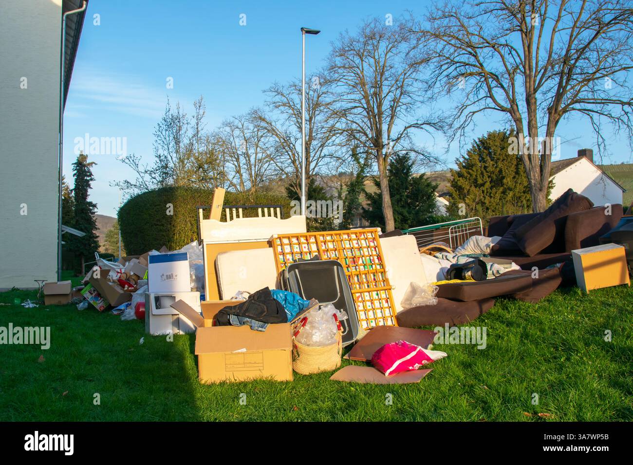 Beaucoup de déchets dans une ville près de la haus. Grandes ordures avec vieux meubles en bois, jouets, boîtes, sacs en plastique dans une rue et l'herbe verte au printemps ensoleillé tra Banque D'Images