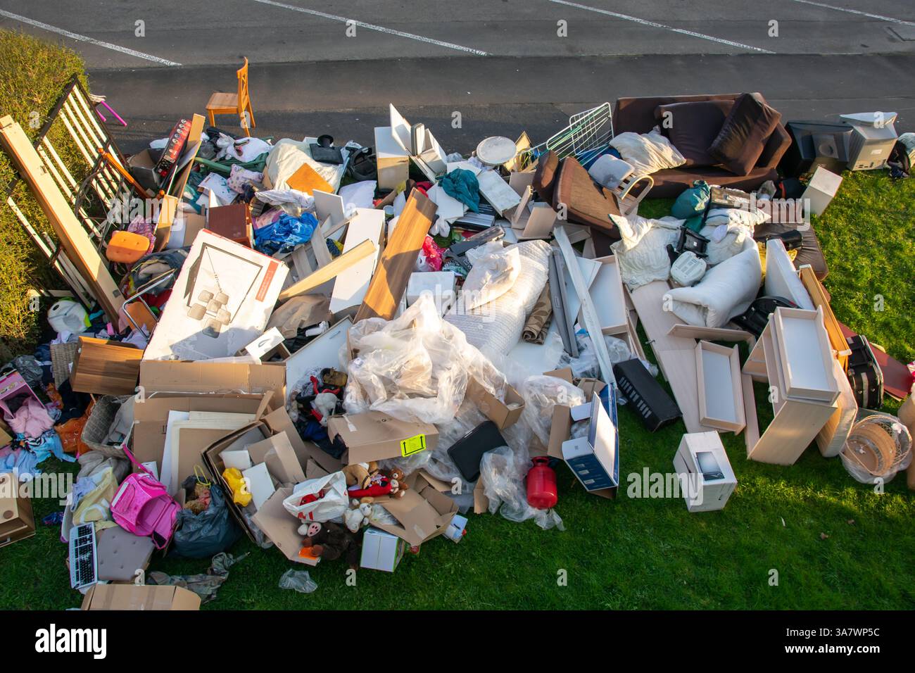 Beaucoup de déchets dans une ville près de la haus. Grandes ordures avec vieux meubles en bois, jouets, boîtes, sacs en plastique dans une rue et l'herbe verte au printemps ensoleillé tra Banque D'Images