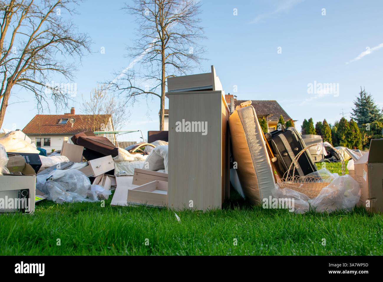 Beaucoup de déchets dans une ville près de la haus. Grandes ordures avec vieux meubles en bois, jouets, boîtes, sacs en plastique dans une rue et l'herbe verte au printemps ensoleillé tra Banque D'Images