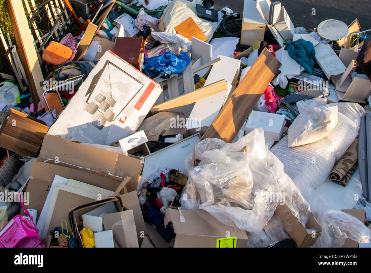 Beaucoup de déchets dans une ville près de la haus. Grandes ordures avec vieux meubles en bois, jouets, boîtes, sacs en plastique dans une rue et l'herbe verte au printemps ensoleillé tra Banque D'Images