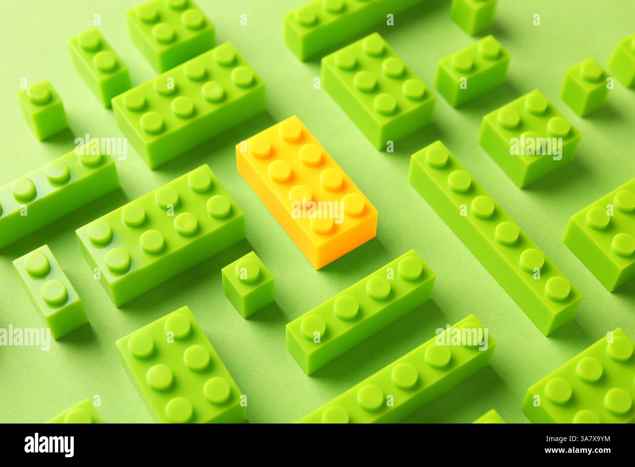 Différence, unicité, individualité. Bloc de construction jaune parmi les verts sur fond de couleur Banque D'Images