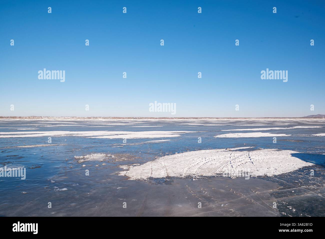 Lac gelé avec chaîne de montagnes et village Banque D'Images
