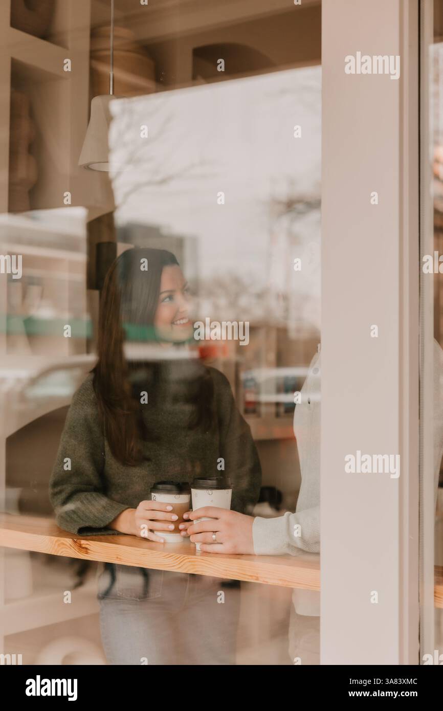Couple tenant des tasses à café, reflétées par une fenêtre de café Banque D'Images Couple tenant des tasses à café, reflétées par une fenêtre de café Banque D'Images