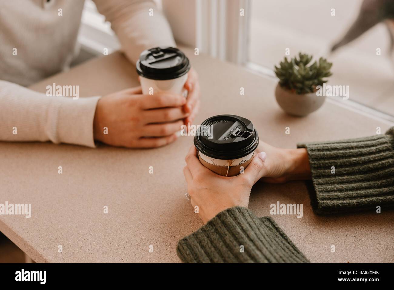 Gros plan de deux personnes tenant des tasses à café à une table près d'une fenêtre Banque D'Images Gros plan de deux personnes tenant des tasses à café à une table près d'une fenêtre Banque D'Images