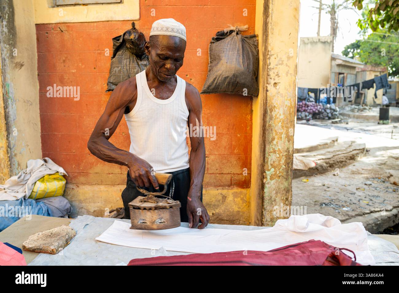 Homme repassage au fer chauffé au charbon, Kofar Mata Dye Pits, Kano, Nigeria Banque D'Images