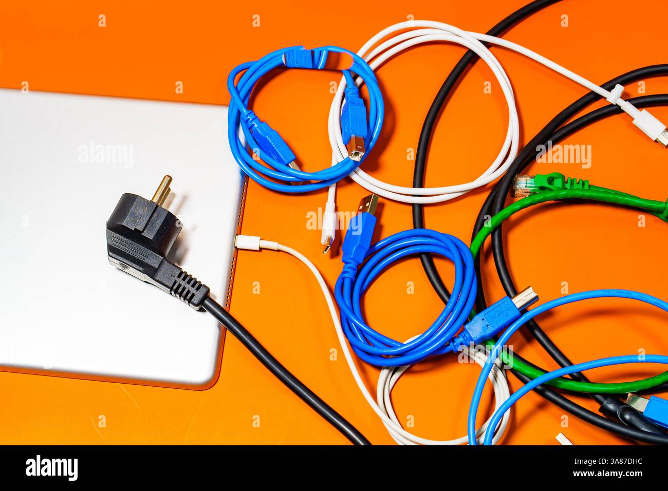 Appareil électronique avec un bouquet de fils colorés sur une table orange. Banque D'Images