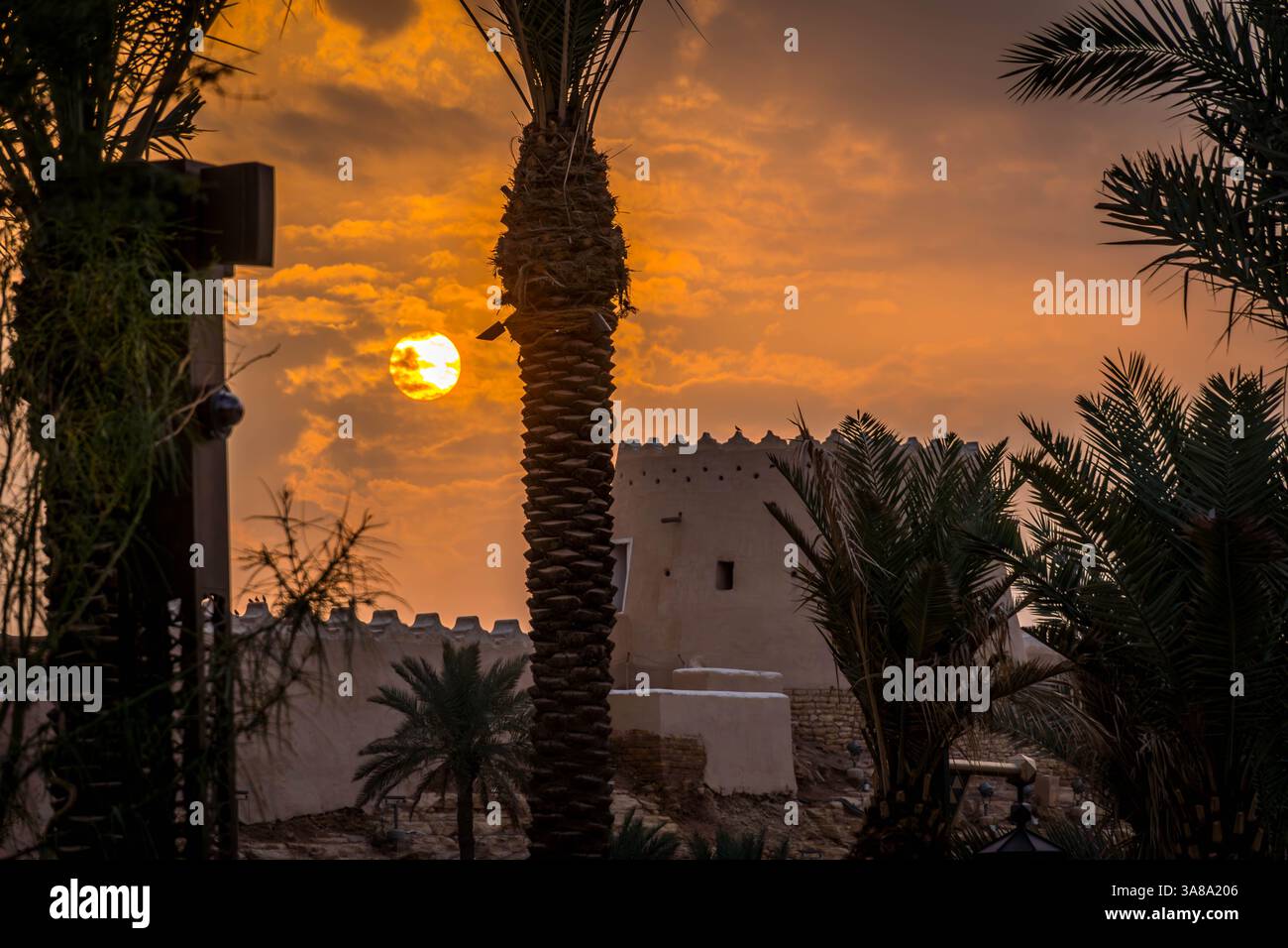 Le soleil jaune derrière le palmier et la forteresse saoudienne avec le ciel nuageux spectaculaire pendant le coucher de soleil chaud de l'été. Banque D'Images