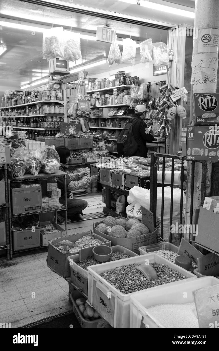 Un client navigue pendant que le personnel réapprovisionne les étagères basses d'un marché local très fréquenté et bien approvisionné. Banque D'Images