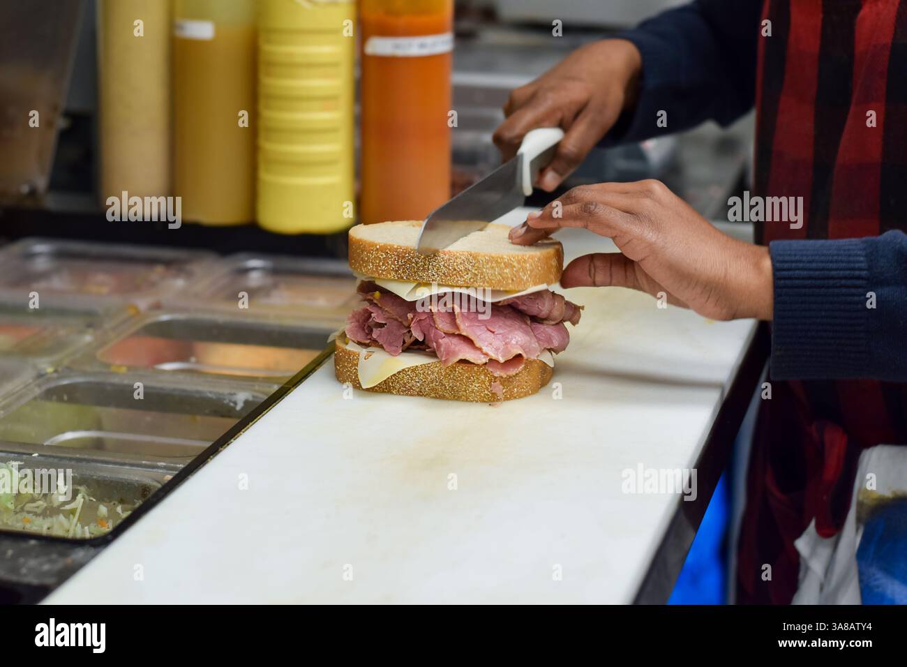 Mains de l'employée de restaurant de diner femelle coupant le sandwich de viande corned Beef de charcuterie en deux avec un couteau Banque D'Images