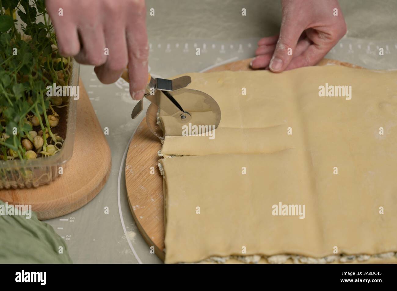 Fermez la feuille carrée de pâte coupée en bandes avec les mains de la femme sur une planche de bois. Couteau, serviette verte, germes microverts sur la table de cuisine. Fait maison Banque D'Images