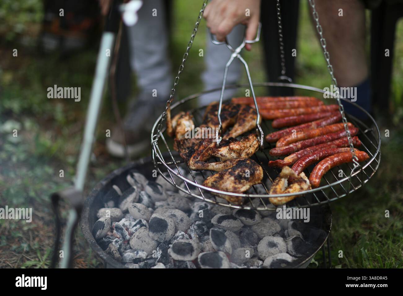 Barbecue d'été dans la cour arrière avec des saucisses et de la viande sur un gril rond - une main tendue, ajoutant à la scène grésillante. Banque D'Images