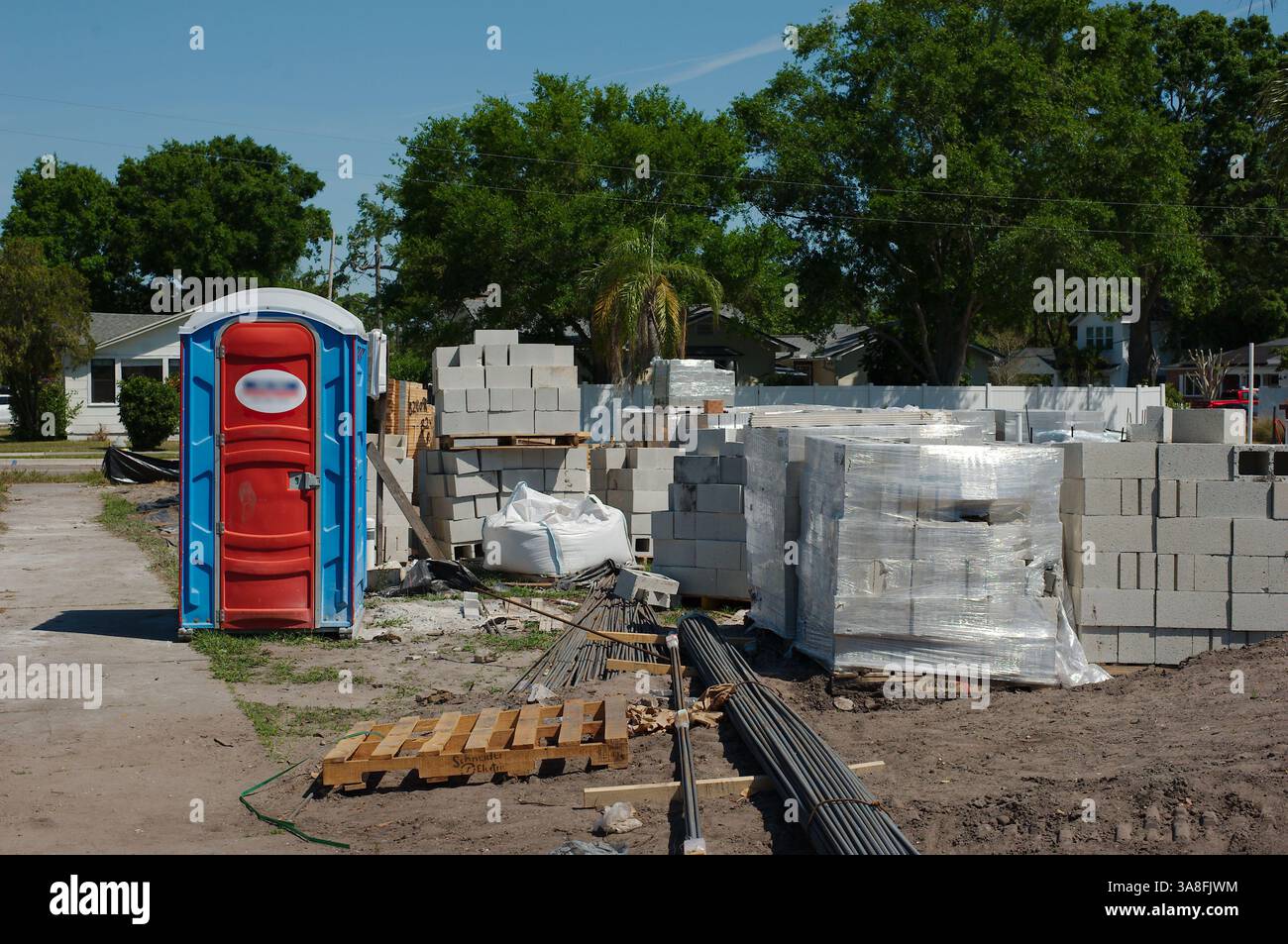Chantier de construction de la maison avec divers matériaux et équipements. Une toilette portative avec une porte rouge et un cadre bleu est visible sur la gauche. Piles de concre Banque D'Images