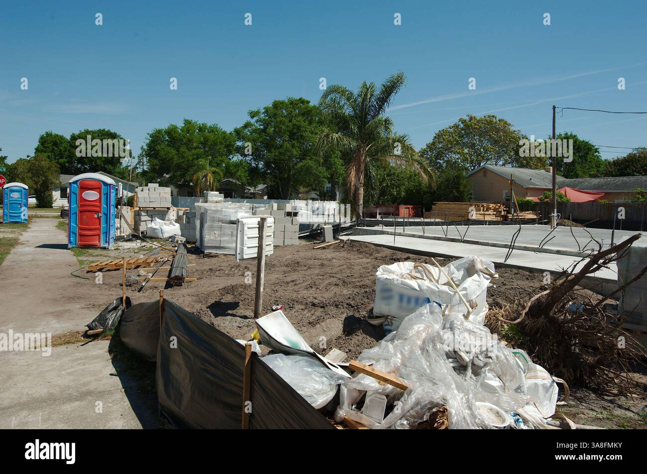 Chantier de construction de la maison avec divers matériaux et équipements. Une toilette portative avec une porte rouge et un cadre bleu est visible sur la gauche. Piles de concre Banque D'Images