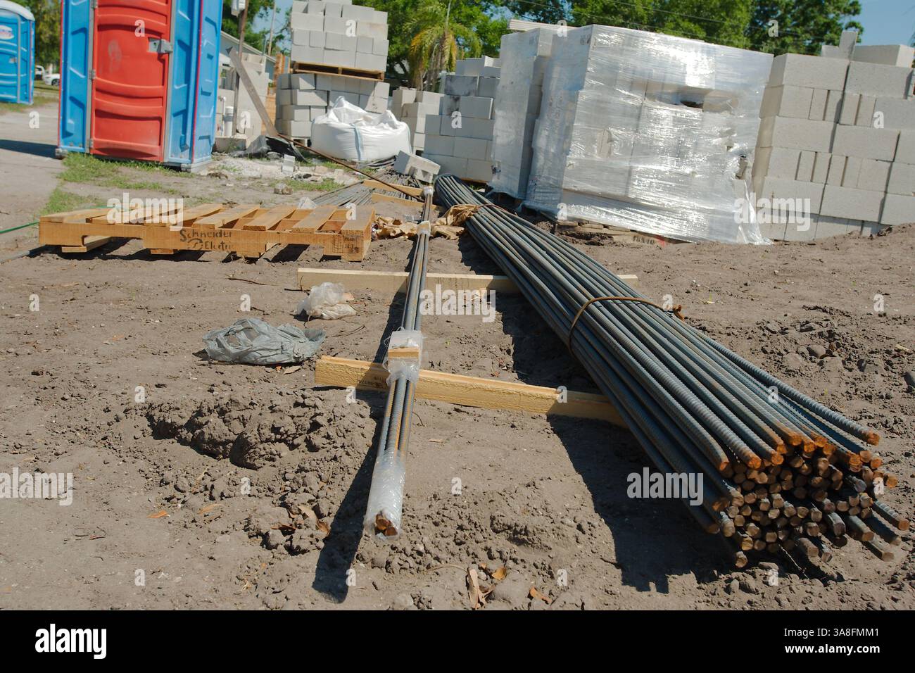 Chantier de construction de la maison avec divers matériaux et équipements. Une toilette portative avec une porte rouge et un cadre bleu est visible sur la gauche. Piles de concre Banque D'Images