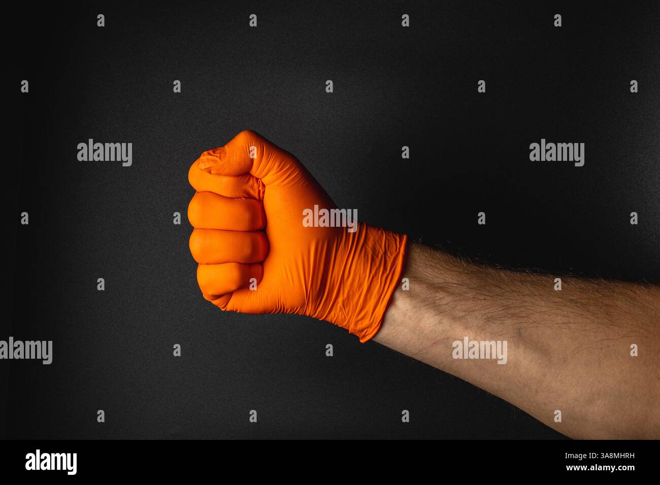 Un poing vêtu d'un gant orange vif est posé sur un fond sombre, représentant la résilience et la puissance dans un contraste visuel saisissant. Banque D'Images